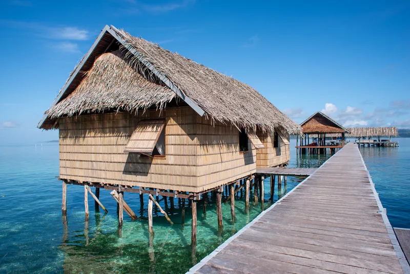 Scenic row of Papuan Water Cottages connected by a wooden footbridge.