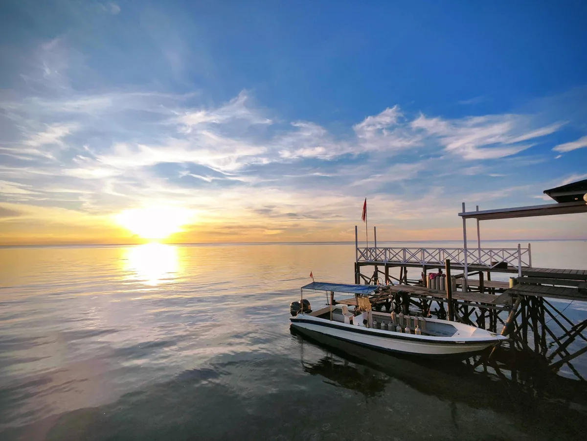A dive boat moored at the jetty as the sun sets over the Celebes Sea.