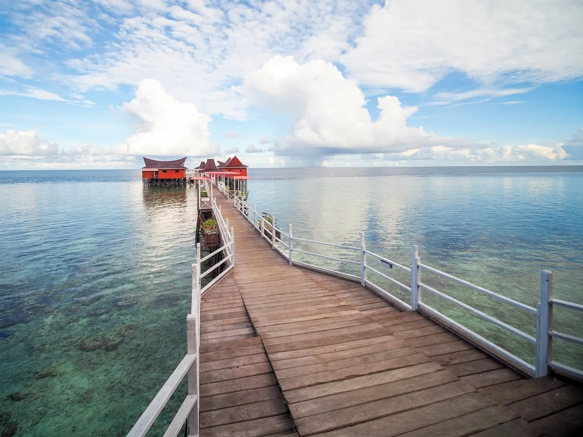 The wooden jetty at Maratua Dive Resort running out over clear water to the overwater dive centre and dining area.